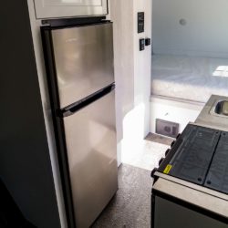 Everchill RV top-freezer refrigerator installed in the galley of a Travel Lite 24SUR toy hauler, next to a sink and two-burner stove.