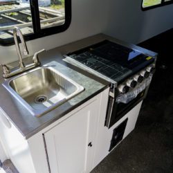 Interior kitchenette of a Modern Buggy Big Buggy teardrop trailer with stainless steel sink, 2-burner range, and 12V refrigerator.