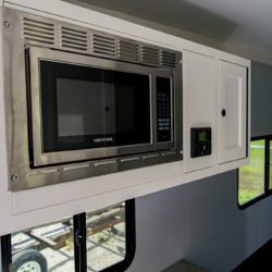 Interior of a Greystone toy hauler RV showing a built-in microwave, cabinetry, and kitchen area.