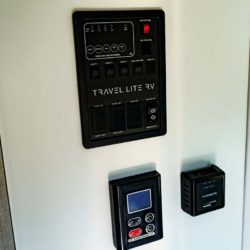 Control panels inside a Travel Lite RV showing switches for lighting and digital controls for climate and water systems.