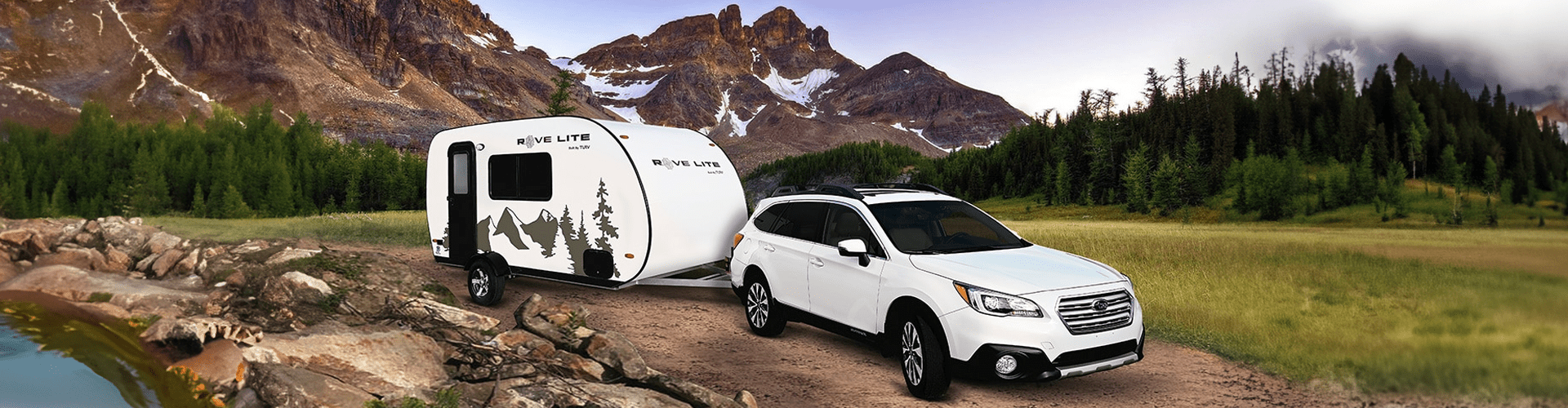 Travel Lite Rove Lite compact travel trailer hitched to a white Subaru SUV, parked on a dirt path with mountains and forest in the background, showcasing easy towing and outdoor adventure readiness.